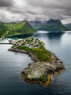 Moody afternoon light on Øyfjorden, looking toward the island that is the village. Husøy is linked to Senja by a 300-meter causeway, about 276 people living on one skerry with its harbor, school, chapel and the little red-roof lighthouse. 

From the fjord side the scale hits you. Steep green walls rise straight from dark water, low cloud sits on the peaks, and the whole community fits in a single frame.

Remote and lived-in at once.

#senja #husøy #northernnorway #djimavic4pro #dronephotography